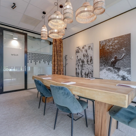 Vergaderruimte op Gustav Mahlerlaan 308 in Amsterdam Zuidas, uitgerust met houten tafel en blauwgroene stoelen onder sfeervolle hangverlichting.