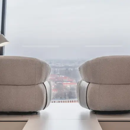 Moderne kantoorruimte met twee comfortabel ogende fauteuils en grote ramen met uitzicht over Amsterdam. Ideaal voor ontspannen vergaderingen of creatieve brainstormsessies in de Zuidas.