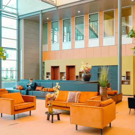 Ruime en lichte lobby in een kantoorpand aan Jachthavenweg 109, Amsterdam Zuidas, met comfortabele zitbanken en planten. Een persoon voert een zakelijke activiteit uit in een hoek.