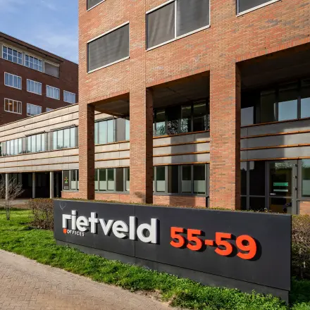 Buitenaanzicht van kantoorpand aan Het Rietveld 55-59 in Apeldoorn, met opvallend bord en moderne uitstraling, ideaal voor kantoorruimte huren.