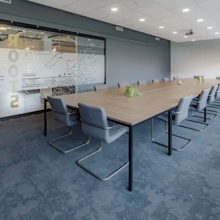 Kantoorruimte huren op Oude Apeldoornseweg 41-45 in Apeldoorn met een moderne vergaderruimte, lange tafel, comfortabele stoelen en glazen deur met opdruk. Ideaal kantoorpand voor vergaderingen.