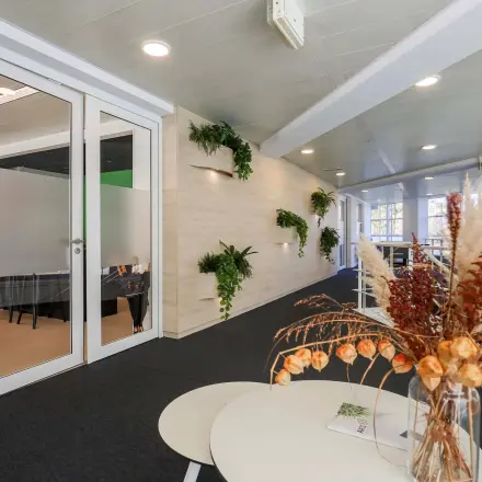 Binnenkant van een kantoorpand op Prins Willem-Alexanderlaan 301 in Apeldoorn, met groen decor en een glazen deur naar een vergaderruimte.