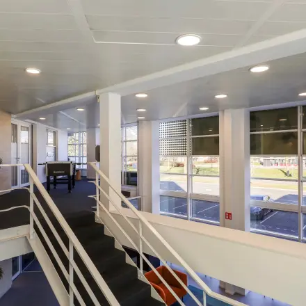 Moderne kantoorruimte huren op Prins Willem-Alexanderlaan 301, Apeldoorn, met ruime ramen en strakke inrichting op de verdieping via een centrale trap bereikbaar.