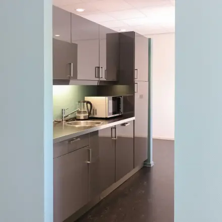 Kantoorruimte huren in Apeldoorn met een moderne, compacte pantry met grijze kasten, een magnetron, en een koffiezetapparaat, gelegen in het kantoorpand aan de Prins Willem-Alexanderlaan 401.