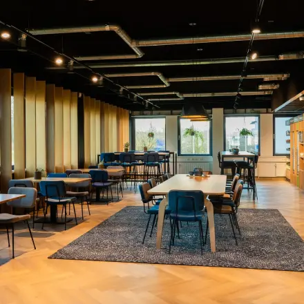 Moderne kantoorruimte met houten vloer, meerdere tafels en stoelen in een open werkopstelling op Prins Willem Alexanderlaan 701, Apeldoorn. Beschikbaar voor kantoorruimte huren.