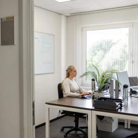 Een licht kantoor op Vlamoven 34 in Arnhem IJsseloord met een bureau, computer en een plant. Een persoon voert werk uit aan het bureau. Ideale ruimte voor kantoorruimte huren.