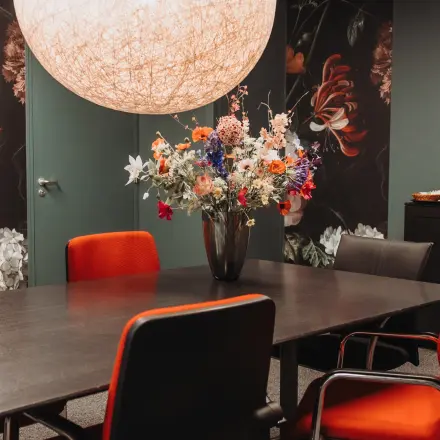 Stijlvolle kantoorruimte huren in Arnhem IJsseloord aan Vlamoven 34 met moderne vergadertafel, felgekleurde stoelen en decoratieve bloemenvaas.