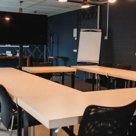 Vergaderruimte in Arnhem IJsseloord met een U-vormige opstelling van houten tafels, zwarte stoelen en een groot scherm. Kantoorruimte huren in kantoorpand op Vlamoven 34, uitgerust voor zakelijke bijeenkomsten.
