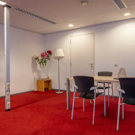 Kantoorruimte huren in Arnhem Zuid aan de Kronenburgsingel 525 met een rode vloerbedekking en enkele stoelen rondom een tafel.
