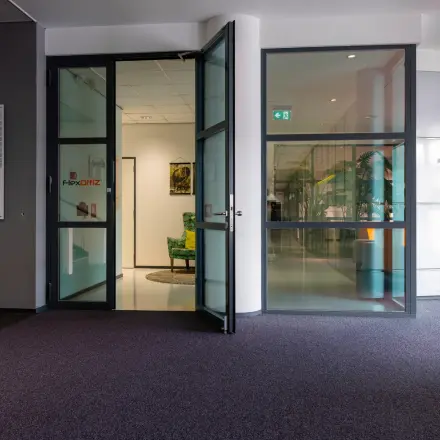 Entree van het kantoorpand op Amalialaan 126 in Baarn met glazen deuren en groene planten, ideaal voor kantoorruimte huren.