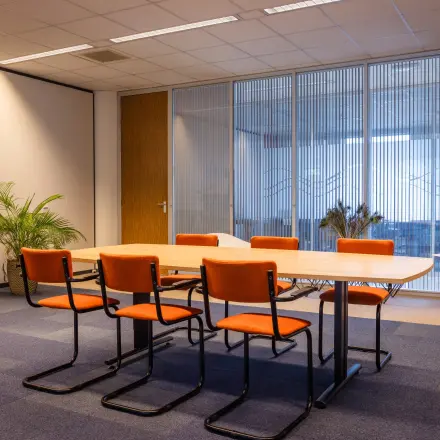 Kantoorruimte huren op Amalialaan 126 in Baarn met een vergadertafel en oranje stoelen, omringd door rustige decoraties en een glazen wand.