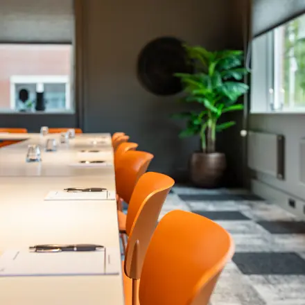Moderne kantoorruimte met feloranje stoelen en een lange tafel, klaar voor bespreking of vergadering. Ideaal voor wie een kantoorpand wil huren in Barneveld.