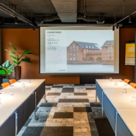 Vergaderruimte in Barneveld met meerdere tafels, stoelen en een groot scherm, ideaal voor kantoorruimte huren. Modern kantoorpand aan Baron van Nagellstraat 136, ruim en functioneel in gebruik.