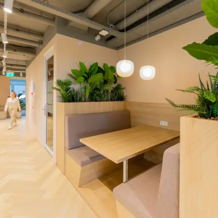 Moderne kantoorruimte huren in Barneveld op Baron van Nagellstraat 136 met groene planten, houten tafels en vloeren. Een persoon loopt door de gang.