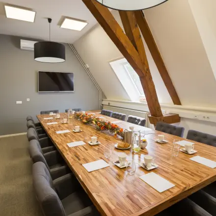 Vergaderruimte in een kantoorpand op Blokstallen 2B, Bergen op Zoom. Ruime tafel met luxe stoelen en groot raam, ideaal voor kantoorruimte huren. Modern ingericht met warme accenten.