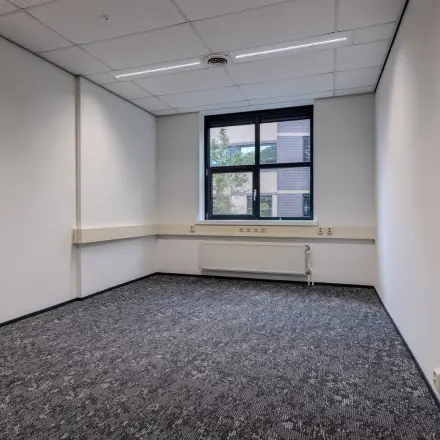 Lege kantoorruimte met tapijtvloer en een raam, ideaal om te huren als werkplek aan de Rijtuigweg 10 in Bergen op Zoom.