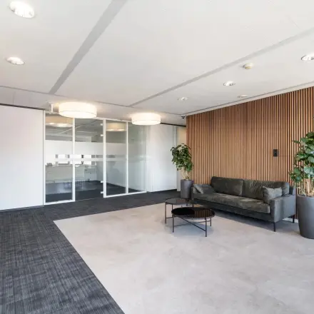 Moderne kantoorruimte op Tolnasingel 1 - 3 in Bodegraven, met glazen wanden, houten wandbekleding en een stijlvolle bank. Ideaal voor wie een kantoorpand wil huren.