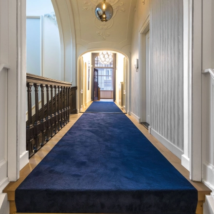 Entreehal van een kantoorpand op Catharinastraat 16 in Breda Centrum-Station met luxe blauwe loper en houten trapleuning, ideaal voor een representatieve entree bij het huren van kantoorruimte.