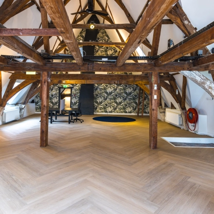 Open kantoorruimte met zichtbare houten balken en visgraatvloer in het kantoorpand aan de Catharinastraat 16, Breda Centrum-Station, beschikbaar voor huur.