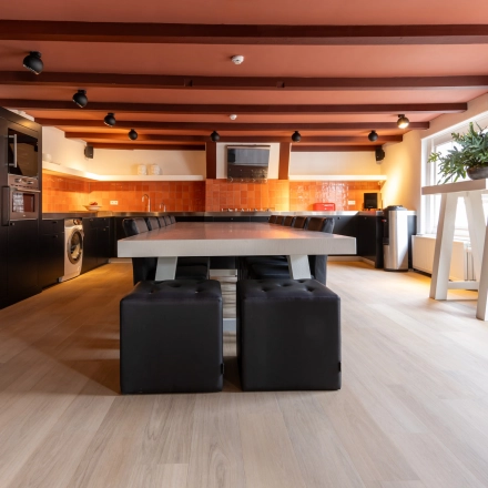 Moderne kantoorruimte huren in Breda met grote houten tafel, comfortabele zitplaatsen en goed uitgeruste keuken in industriële stijl gelegen aan Catharinastraat 16, Breda Centrum-Station.