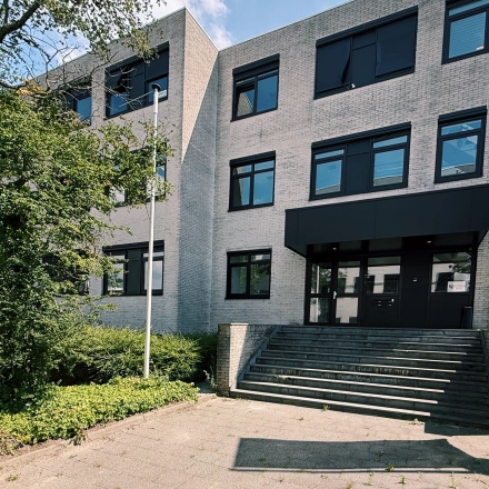 Het kantoorpand aan de Druivenstraat 25-31 in Breda Oost, geschikt voor kantoorruimte huren. De moderne gevel met grote ramen is omgeven door groen en betegelde paden.