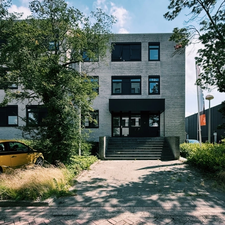 Entree van kantoorpand aan de Druivenstraat 25-31 in Breda Oost, met bomen en een geparkeerde auto voor de ingang.