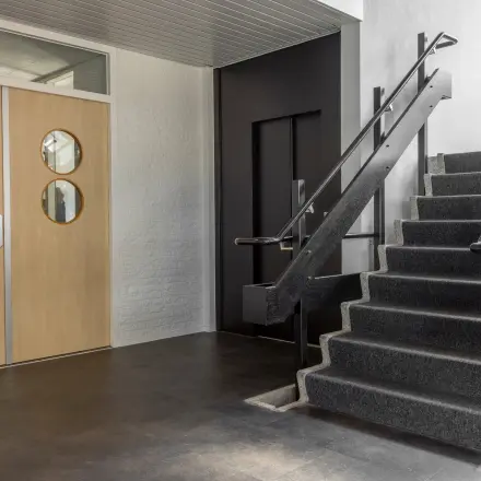 Ingang van het kantoorpand op Druivenstraat 25-31 in Breda Oost, met een strakke trap en moderne deuren. Licht valt binnen via grote ramen.