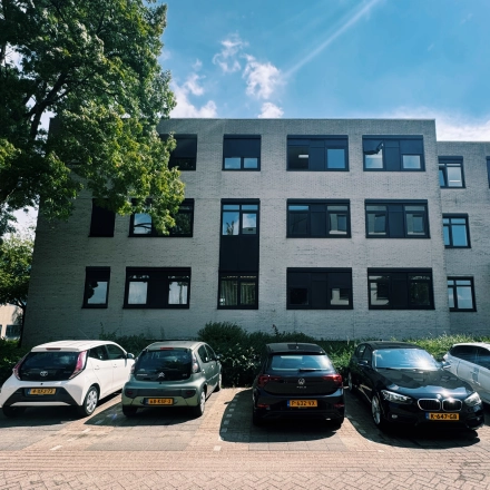 Moderne kantoorpand aan Druivenstraat 25-31 in Breda Oost met meerdere parkeerplaatsen aan de voorzijde onder een blauwe hemel.