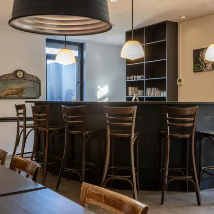 Een moderne kantoorruimte te huur in Breda Oost aan de Druivenstraat 25-31. Het interieur is voorzien van hoge houten stoelen aan een bar en een tafel. De ruimte is uitnodigend en functioneel.