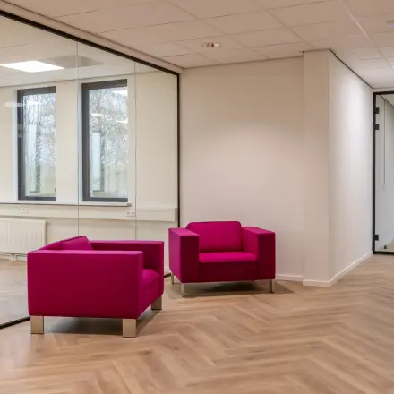 Een lichte kantoorruimte op Vlierbaan 20, Capelle aan den IJssel, met glazen wanden en twee roze fauteuils, ideaal voor het huren van een stijlvol kantoorpand.