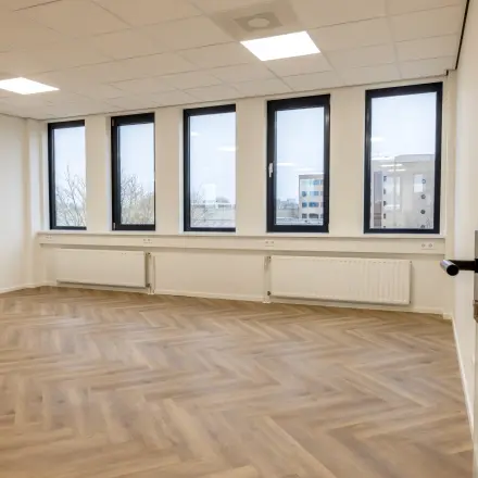 Lichte kantoorruimte aan Vlierbaan 20, Capelle aan den IJssel, met grote ramen voor natuurlijk licht, ideaal voor huur. Houten vloer in visgraatpatroon geeft het kantoorpand een stijlvolle touch.