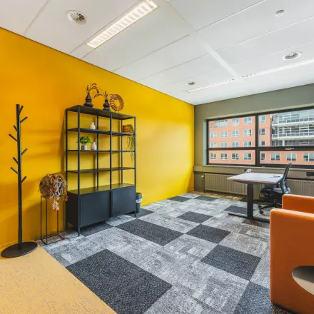 Kantoorruimte huren in De Meern op Rijnzathe 12 met kleurrijke muren en grote ramen. Het kantoor is ingericht met een bureau, stoel en kast. Modern en uitnodigend voor zakelijke activiteiten.