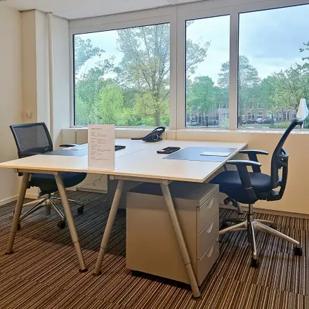 Kantoorruimte te huur aan Poortweg 4 in Delft met een lichte werkplek voorzien van twee bureaus en stoelen, uitzicht op groene omgeving.