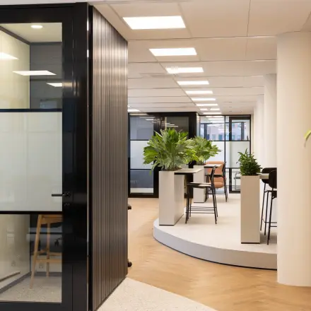 Moderne kantoorruimte met glazen wanden en groene planten op Hambakenwetering 1, Den Bosch. Ideaal om een kantoorpand te huren met stijlvol interieur en ruime werkplekken.
