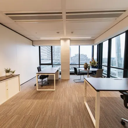 Lichte kantoorruimte op Anna van Buerenplein 41 in Den Haag Centrum met grote ramen, bureaus en stoelen, ideaal voor kantoorpand huur. De ruimte is modern gemeubileerd.