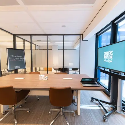 Moderne kantoorruimte te huur in Den Haag Centrum op Anna van Buerenplein 41, met glazen wanden, een grote werktafel, comfortabele stoelen en presentatieschermen.