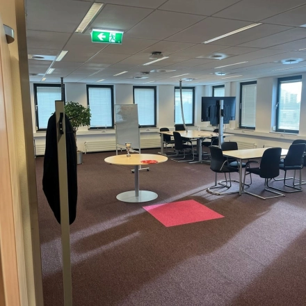 Kantoorruimte in Den Haag Escamp op Platinaweg 10 met grote ramen, een flip-over en meerdere bureau's met stoelen, ideaal voor huren.