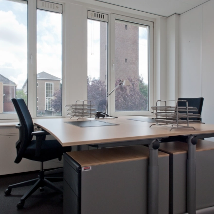 Kantoorruimte huren op Bezuidenhoutseweg 161, Den Haag Haagse Hout. De lichte ruimte heeft een groot raam, twee bureaus met stoelen en een uitzicht op omliggende gebouwen.