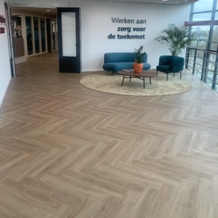 Moderne kantoorruimte met houten vloer, twee blauwe fauteuils en een kleine bank aan Johan de Wittlaan 3-7, Den Haag Statenkwartier. Ruimte biedt volop licht en uitzicht voor bedrijven die kantoorruimte huren.