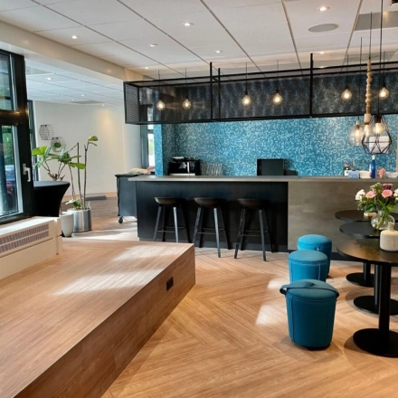 Moderne lounge in kantoorpand op Johan de Wittlaan 3-7, Den Haag Statenkwartier, met zithoek, barkrukken en decoratieve verlichting. Ideaal voor kantoorruimte huren.