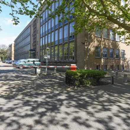 Exterieur van het kantoorpand aan de President Kennedylaan 19 in Den Haag Statenkwartier, met parkeerplaatsen en toegangsweg. Ideaal voor kantoorruimte huren in een groene omgeving nabij voorzieningen.