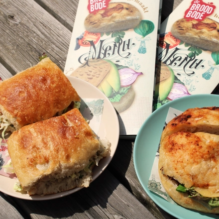 Zonnig terras met houten tafel en smakelijke lunchgerechten zoals broodjes van De Broodbode.