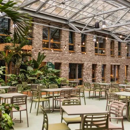 Kantoorpand op Flight Forum 120-159 in Eindhoven Airport met glazen plafond en groene elementen, een ideale plek om kantoorruimte te huren. Ruimte bevat tafels en stoelen in een open setting.
