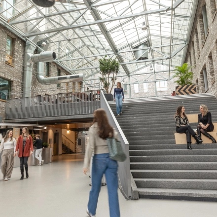 Moderne kantoorruimte met glazen dak op Flight Forum 120-159 in Eindhoven Airport, waar mensen werken en socializen op verschillende niveaus. Ideaal om kantoorruimte te huren in een inspirerende omgeving.