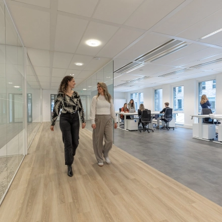 Moderne kantoorruimte huren bij Eindhoven Airport, Flight Forum 120-159. Ruime werkplekken met glazen scheidingswanden en aanwezigheid van medewerkers in overleg.