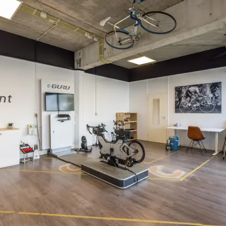 Kantoorruimte te huur op Luchthavenweg 81, Eindhoven Airport. De ruimte heeft een modern interieur met houten vloeren en is deels gemeubileerd. Inclusief werktafel, fietsensimulator en een fiets aan het plafond.