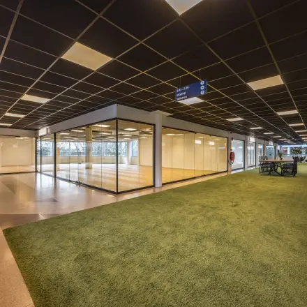 Moderne kantoorruimte te huur op Luchthavenweg 81, Eindhoven Airport, met grote glazen wanden en groene accenten binnen het kantoorpand.