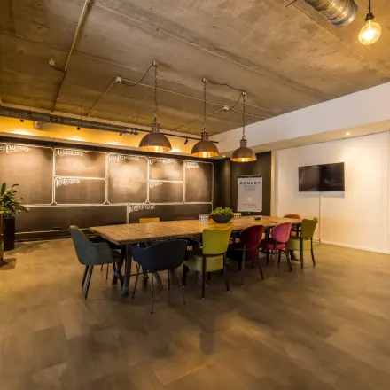 Stijlvolle vergaderzaal met lange houten tafel en gekleurde stoelen, ideaal voor kantoorruimte huren op Eindhoven Airport.