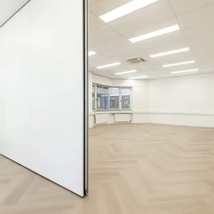 Heldere, open kantoorruimte in Eindhoven De Hurk met grote ramen en houten vloerpatroon, ideaal voor kantoorruimte huren. Flexibele wanden bieden mogelijkheid tot verschillende indelingen.