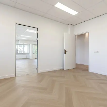 Lege kantoorruimte in Eindhoven De Hurk, te huur met houten vloer en brede openingen naar andere kamers.